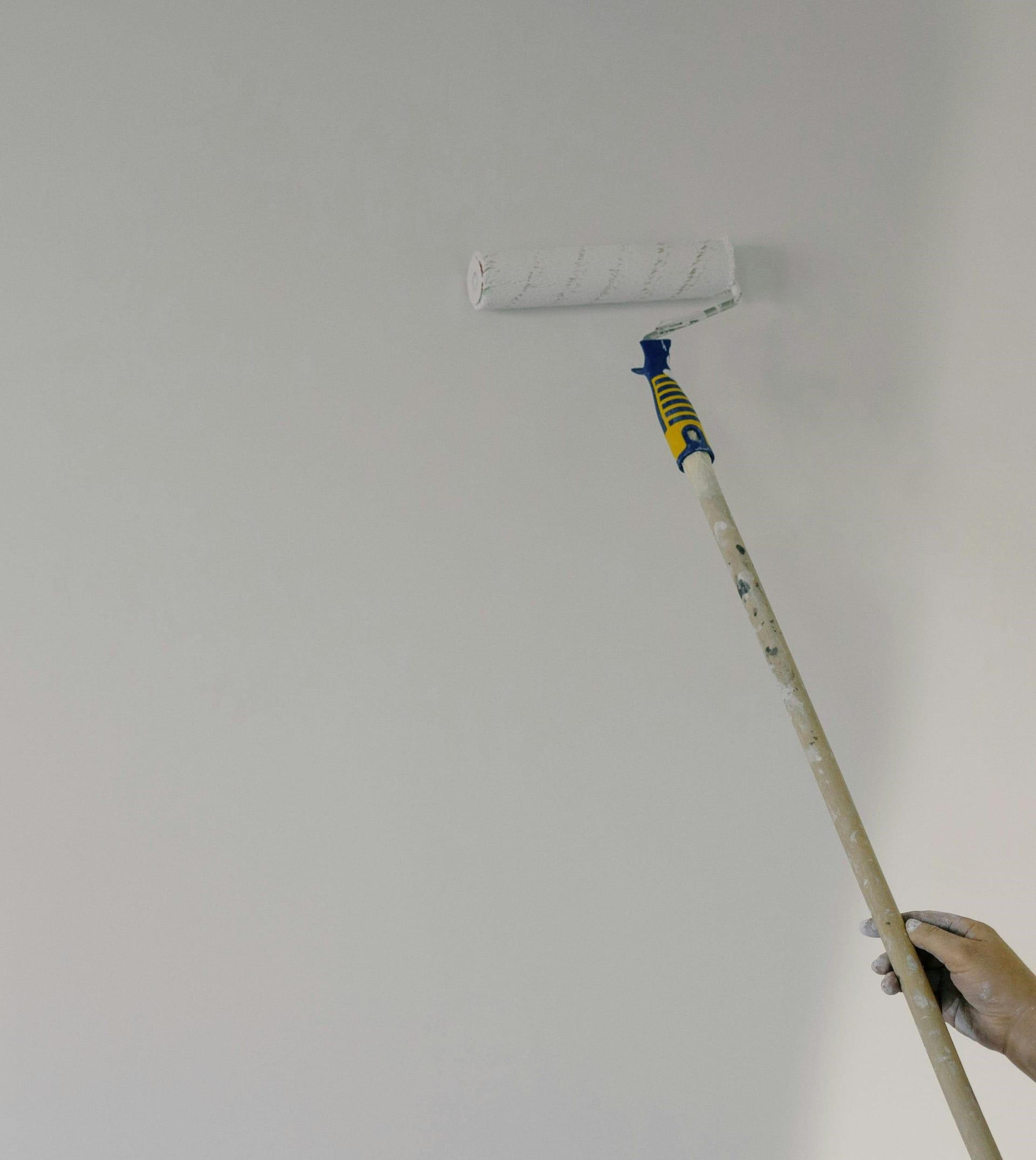 Maler-Roller beim Endanstrich einer hellen Wohnzimmerwand mit Dispersionsfarbe.